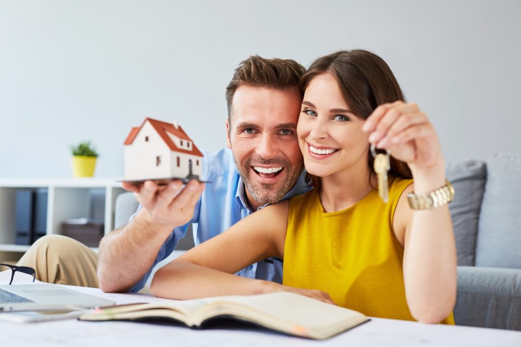 Couple planning to buy a house: showing house keys and miniature house models
