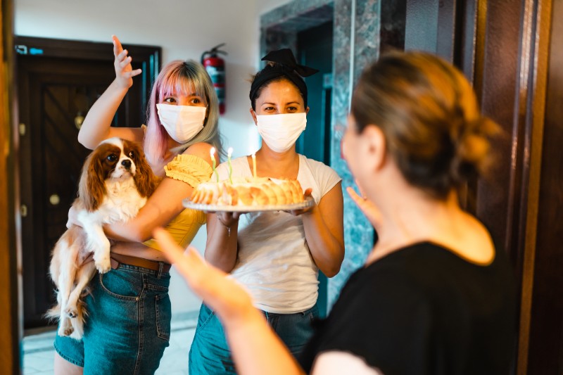 Surpise welcome to a guest with delicious cake with candles while wearing a mask
