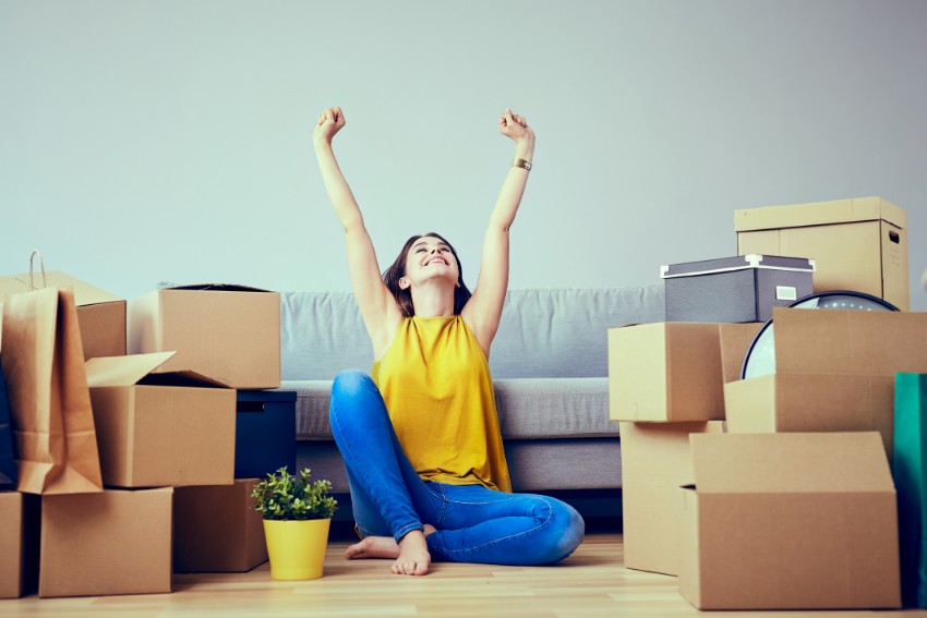 happy woman sitting and raising her hand with boxes around her
